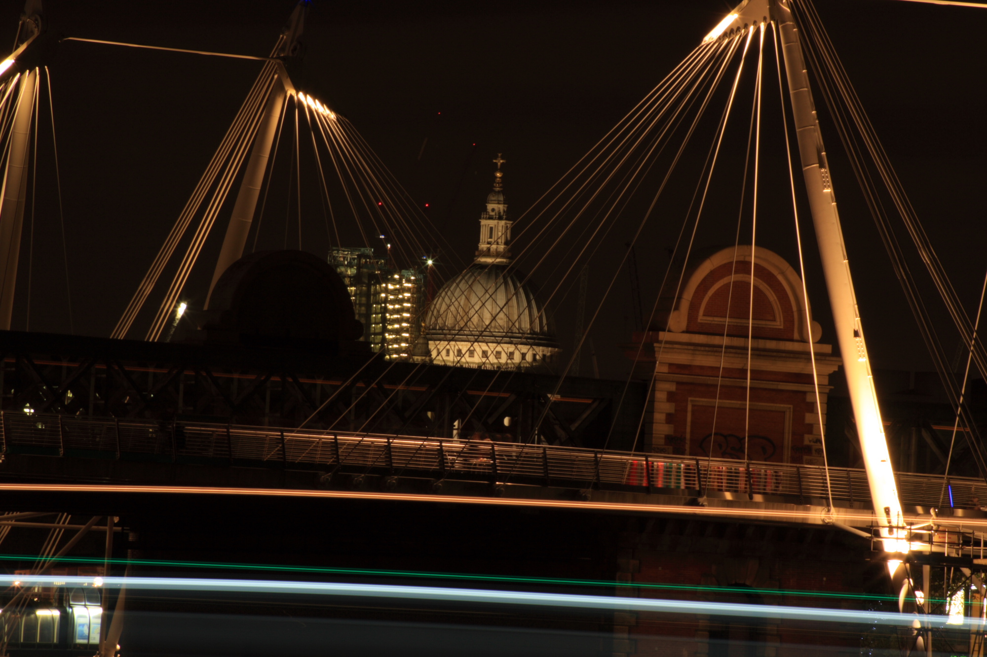 An illuminated St Pauls viewed through an illuminated bridge at night.
